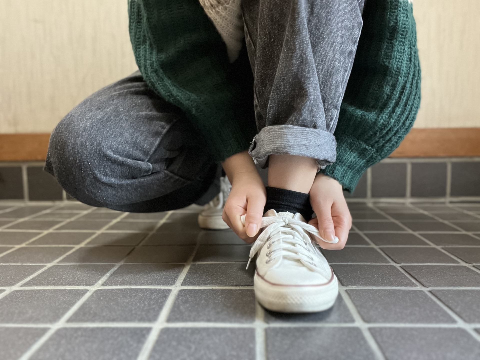明るい玄関でスニーカーを履き外出準備をする女性の足元